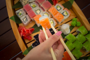 chopsticks in a female hand with a roll. set of rolls on the ship . set sush. Japanese food