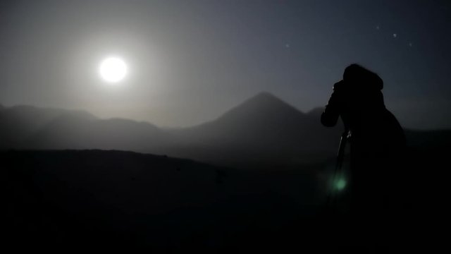 Female photographer taking photos to full moon with the silhouette of the mountains. 4k