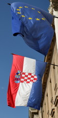 Flagi Chorwacji i Unii Europejskiej powiewają na wietrze, zawieszone obok sie, na zenętrznej ścianie budynku, w tle niebieskie niebo - obrazy, fototapety, plakaty