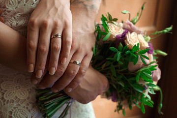 Obraz na płótnie Canvas hands of the bride and groom with wedding rings, bride holds a wedding bouquet in hands, the groom hugs her from behind