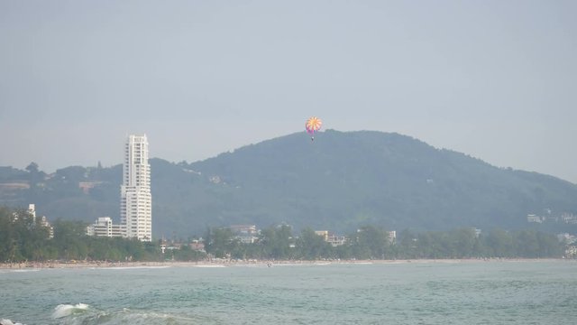 sea wave at Patong sand beach Phuket.  parasail , high building, tree and mountain are  background .