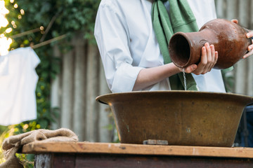 the boy holds a clay jug, pours water out of it into a copper basin. help