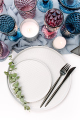 Wedding or festive table setting. Plates, wine glasses, candles and cutlery with gray decorative textile on white background. Beautiful arrangement.