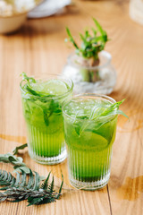 Green lemonade with tarragon, lime and ice on wooden background