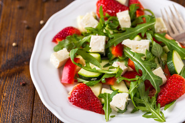 Fresh vegetable strawberry salad on white plate on natural rustic desk.