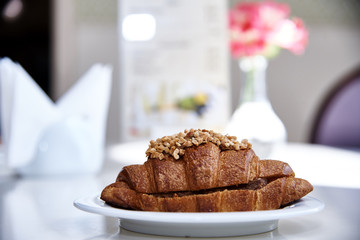 Croissant with a filling on a white plate on a table with flowers in the sunlight.