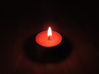 A small red tealight candle lit in a dark room on a table