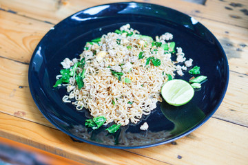 Close-up stir fried Mama or Thai phat  fried noodles with sliced lemon and vegetables in black dish, On the Oak wooden table background.
