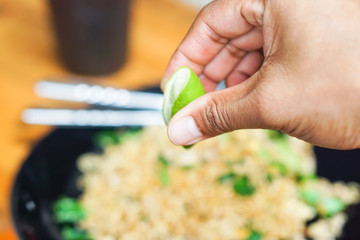 Men's hands are squeezed lime into blurred stir fried Mama or Thai phat  fried noodles in black dish.