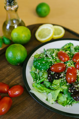 Fresh salad from different kinds of greens and a cherry tomato, dressed with olive oil and sprinkled with sesame seeds
