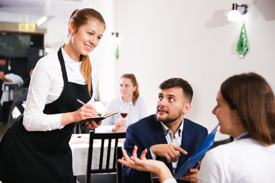 Welcoming female waiter is taking order from couple in restaurante