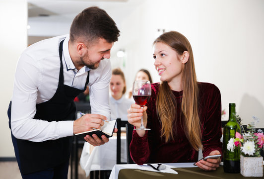 Waiter is taking order from young female in restaurante