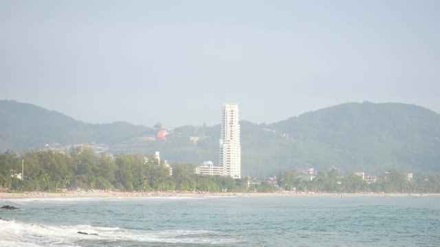 sea wave hit the rock shore seascape , Patong sand beach Phuket  parasail , high building, tree and mountain are  background ,