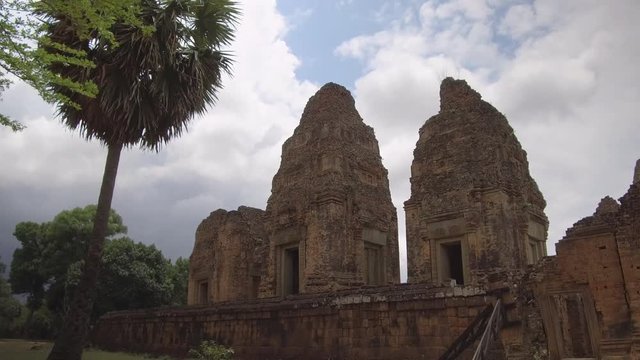 Walking along the stone walls of decaying ancient Buddhist temples in Cambodia, hidden in remote forest. Spectacular shot of big temple complex from ancient times. Beautiful forgotten old buildings.