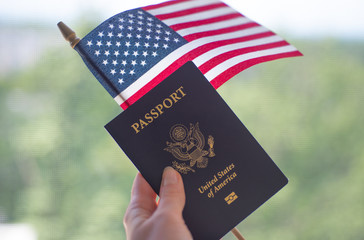 Passport of USA and American Flag in hand. Blurred background.