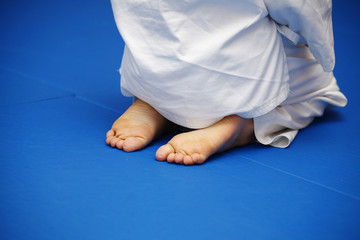 A boy in a white kimono sits on a blue tatami during a workout. Feet