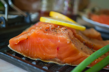 A large piece of salmon marinated with lemon lies on a wooden table for cooking. Horizontal frame.