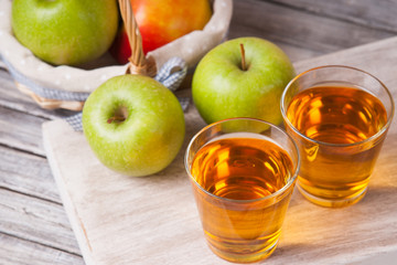 Apple juice in glasses and apples in a wicker basket on wooden table 