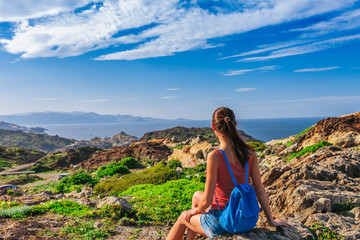 Naklejka na ściany i meble Tourist woman with backpack on Cap de Creus, natural park. Eastern point of Spain, Girona province, Catalonia. Famous tourist destination in Costa Brava. Sunny summer day with blue sky and clouds