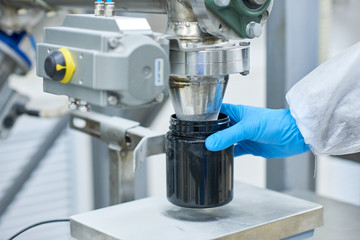 Crop close-up production worker hand in protective glove filling black container with sports...