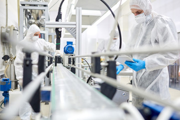 Sports nutrition production workers in protective clothing operating at conveyor belt. 