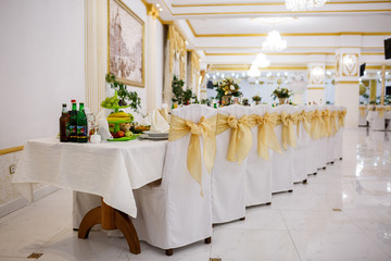 Beautifully organized event, glasses at served festive white table ready. Event in restaurant. Banquet, wedding decor, celebration. Catering and event. Wedding tables. Large restaurant hall.