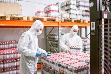 Sports nutrition production employees in protective clothing unloading packs of plastic bottles in warehouse.