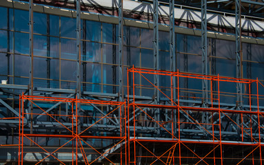 Fototapeta na wymiar Orange falseworks in front of the modern bilding fully covered with glass windows. Concept of repairing and renovating the house