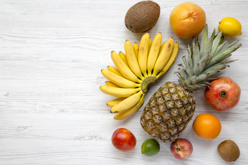 Set of fresh tropical fruits over white wooden background, top view. Copy space. Summer pattern.
