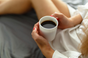 Slim, perfect and beautiful woman drinking her coffee while sitting on bed. Sunny Lazy morning in bed. Cropped image of erotic lying on the bed of a girl in the bedroom. Top view.