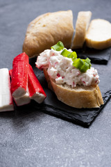 Appetizer with surimi sticks and mayonnaise served on a black slate tray. 