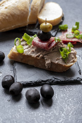 Bread with pate on the black slate tray decorated with black and green olives