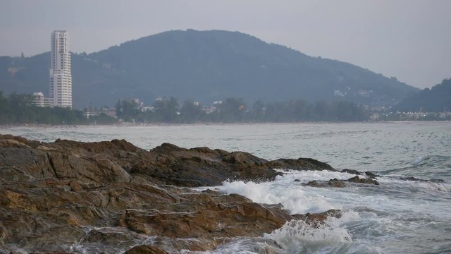 sea wave hit the rock shore seascape , Patong sand beach Phuket  parasail , high building, tree and mountain are  background ,