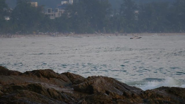sea wave hit the rock shore seascape , Patong sand beach Phuket  jetski, parasail , high building, tree and mountain are  background ,