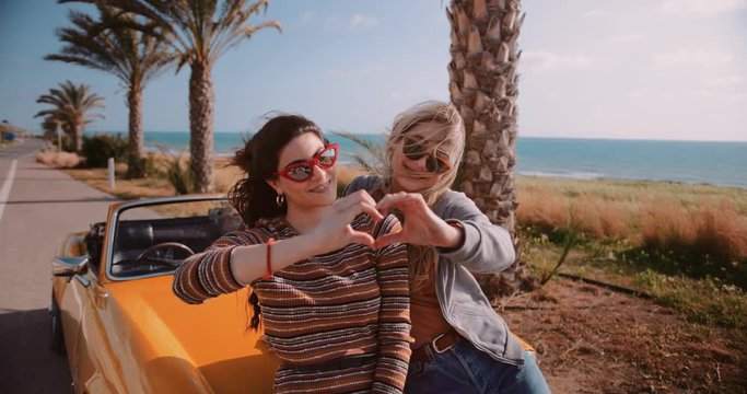 Women with retro convertible car making heart shape with hands