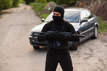 The terrorist in a black mask with an automatic weapon in his hands stands on the background of a...