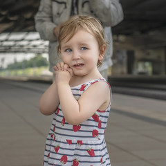  little girl with blue eyes and blond hair on the railway platform looks sadly into the distance.