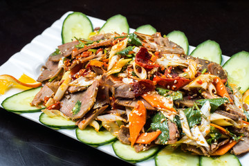 Chinese cuisine, boiled beef with cucumber and tomato in white plate, on black background