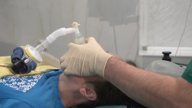 Patient with anesthesia mask in surgical room, anesthesiologist working in operating room