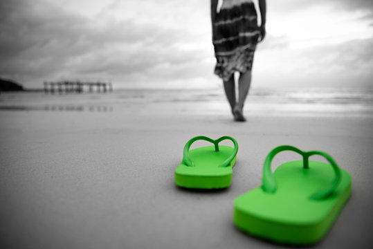 Soft focus on Green flip flop  with sad woman walking on sandy beach. black and white photo.