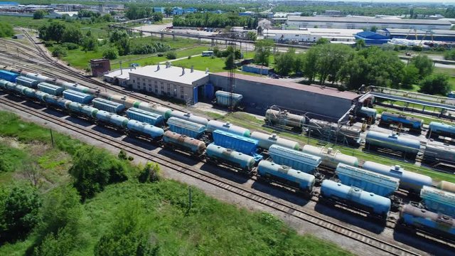 Aerial view of a large train of tanks on the rails next to the production buildings. The camera flies over a long train of tanks standing on the rails.