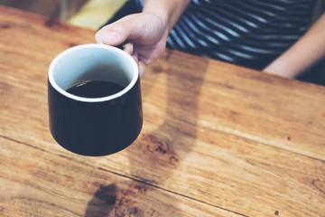 Closeup image of woman's hands holding a black coffee on wooden vintage table