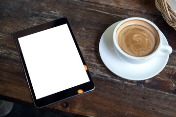 Top view mock up image of black tablet with white blank desktop screen and coffee cup on vintage wooden table in cafe