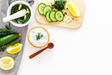 Greek yogurt as salad dressing. Bowl with yogurt, greenery, cucumber, oranges on cutting board on white kitchen desk top view copy space