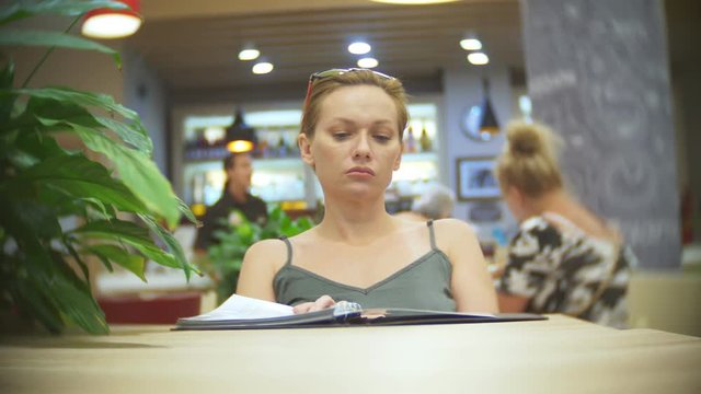 Woman looking at menu in restaurant, turning pages and choosing plates for dinner lunch event dating, 4k, slow motion