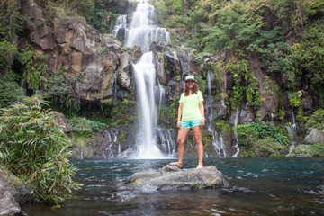 Woman model stands in front of a tropical waterfall long exposure