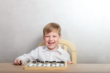 cheerful happy child playing checkers at the table