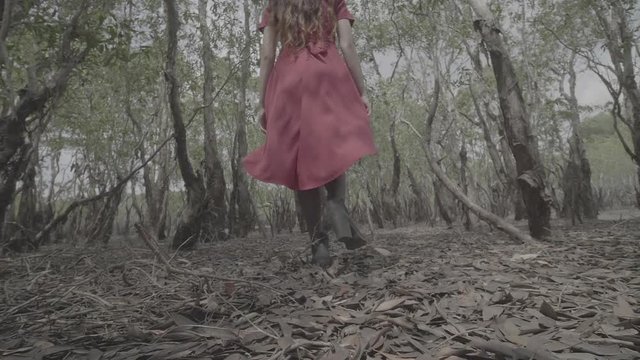 Wide shot of girl in red dress running in mangrove forest in Terengganu, Malaysia.
