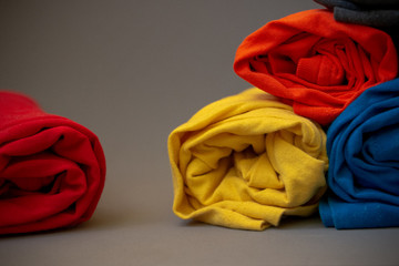 Stack of colorful rolled t-shirts on gray background.