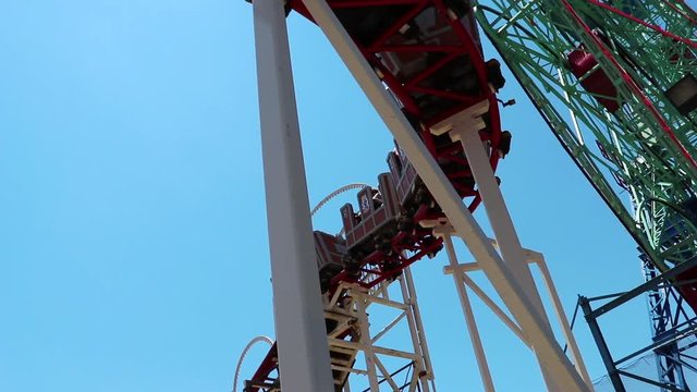 Coney Island Roller Coaster in high definition, slow motion making a turn above the camera. You can see a brief moment of the sun peeking through in between cars.
